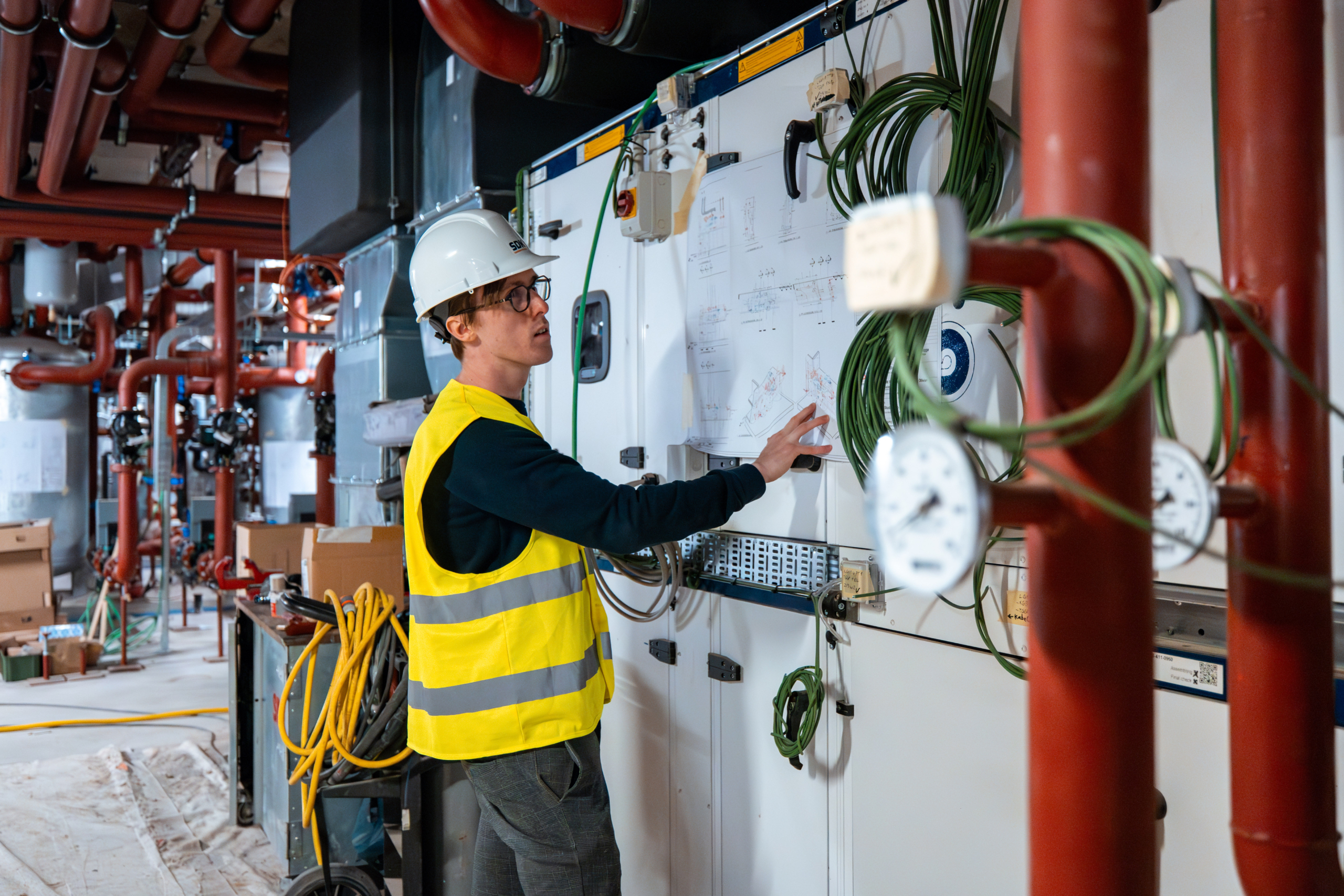 Technicus in fluohesje controleert een schakelkast in een technische ruimte