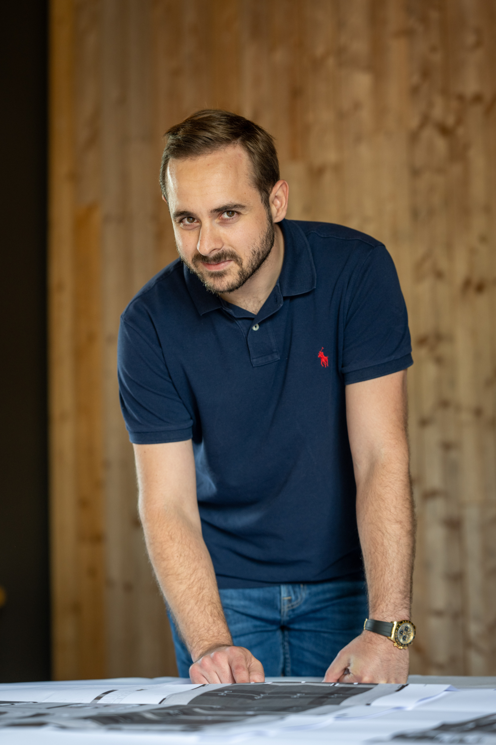 Portret van een man in donkerblauwe polo, leunend over bouwplannen