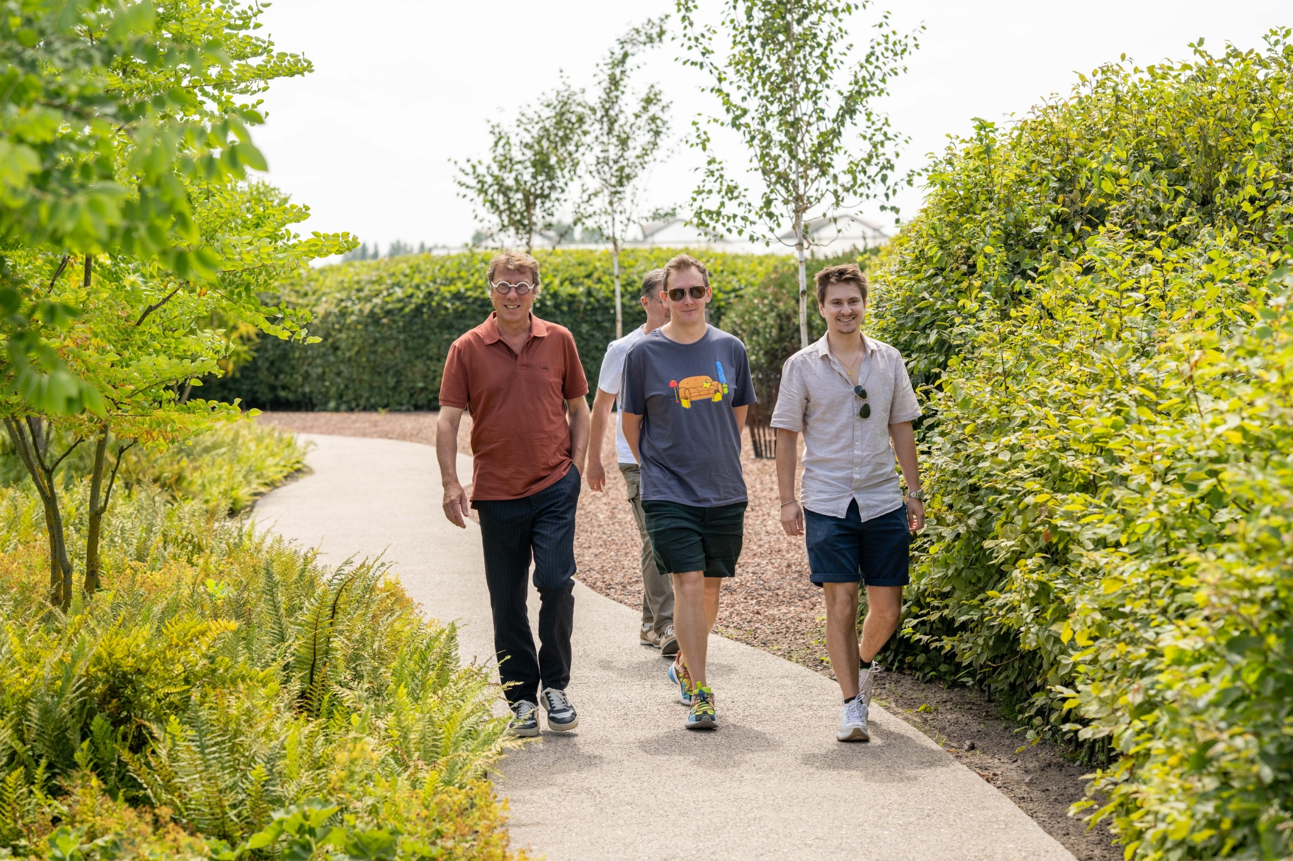 Drie collega’s wandelen over een tuinpad tussen het groen
