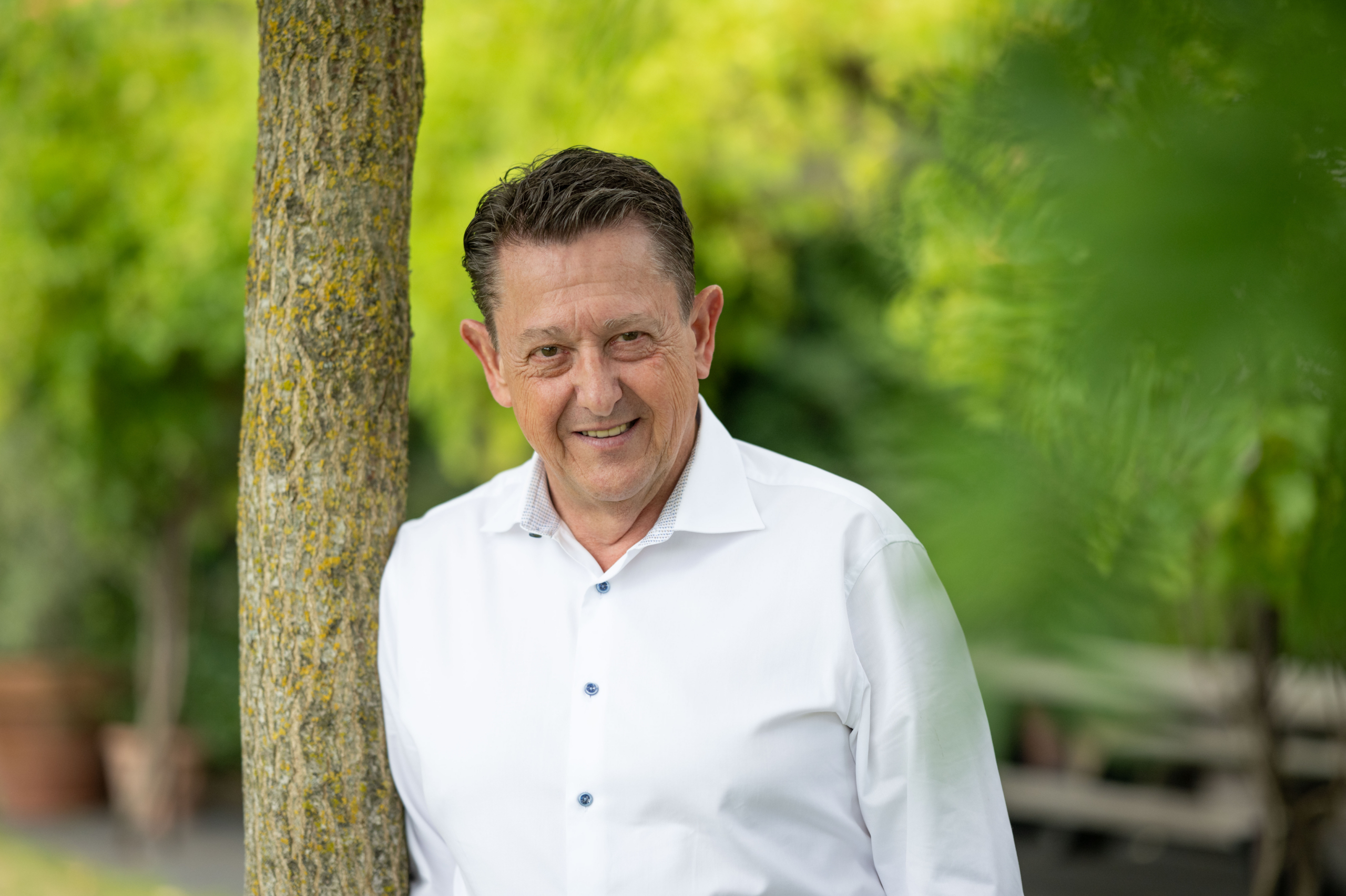 Portret van een man in wit hemd, leunend tegen een boom