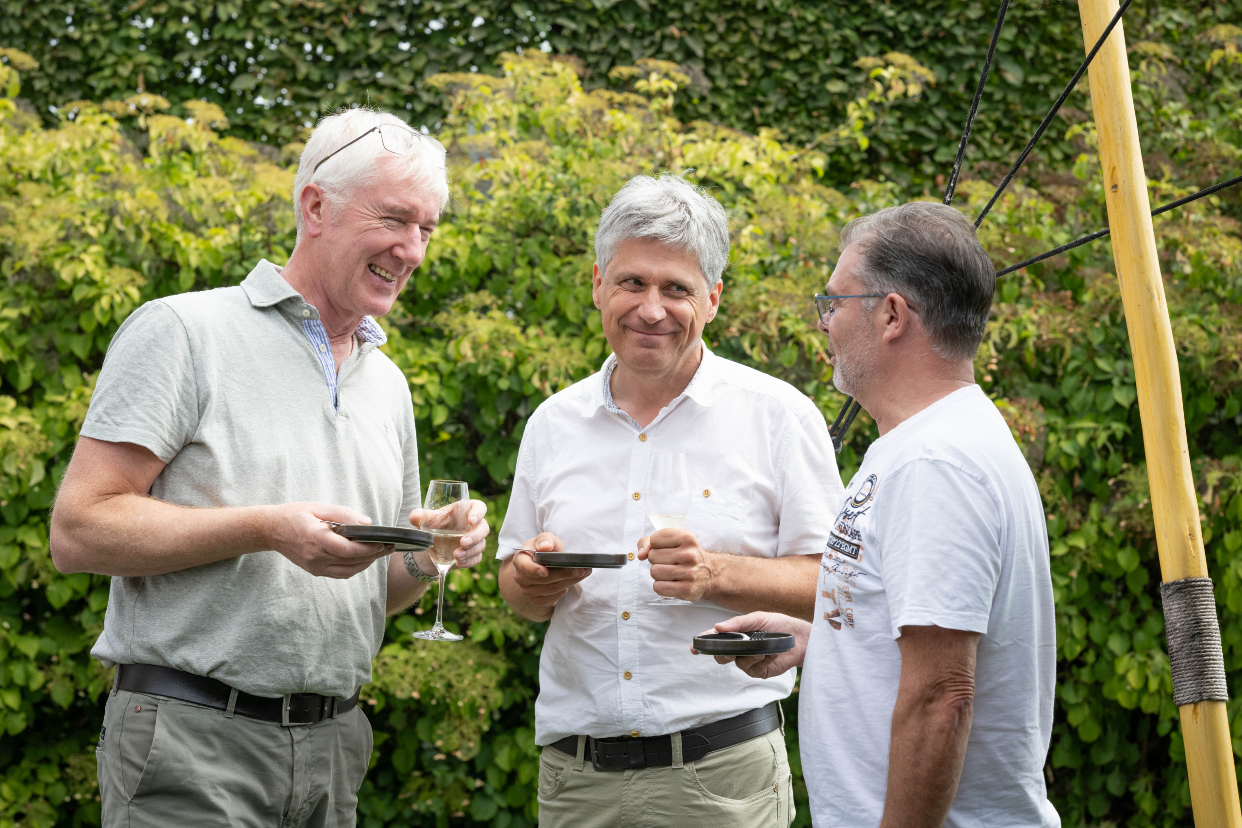 Drie mannen lachen samen tijdens een receptie in de tuin