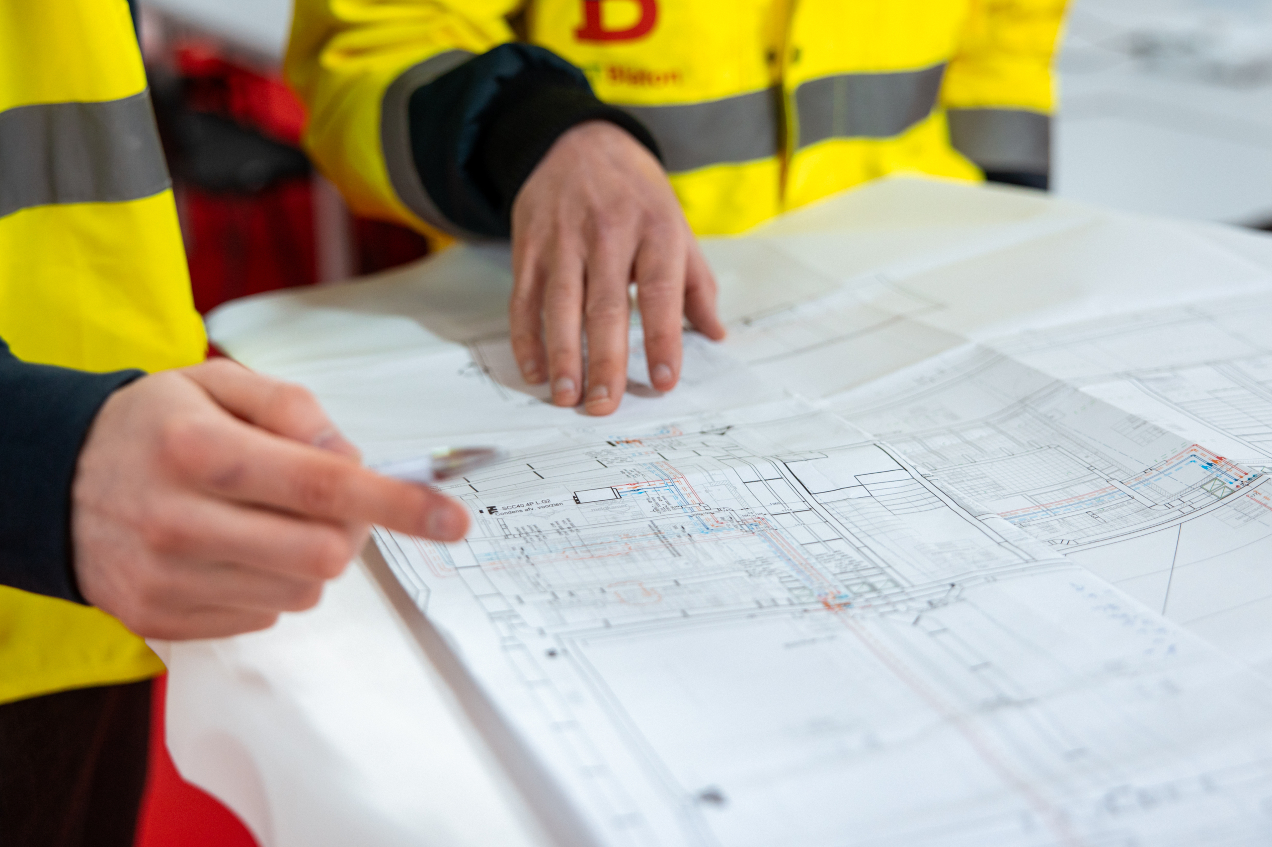 Twee personen in werfkledij overlopen een bouwplan