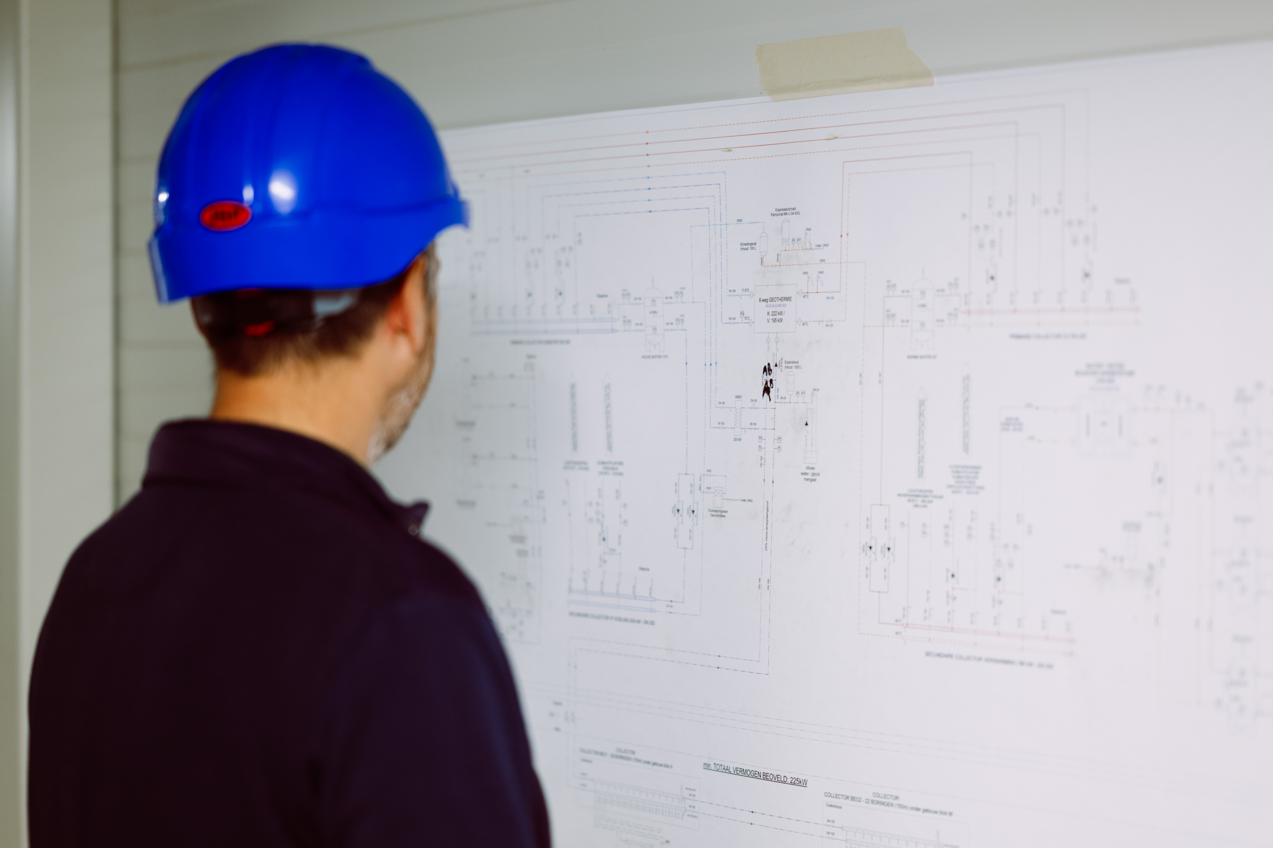 Ingenieur met blauwe helm bestudeert een technisch schema aan de wand