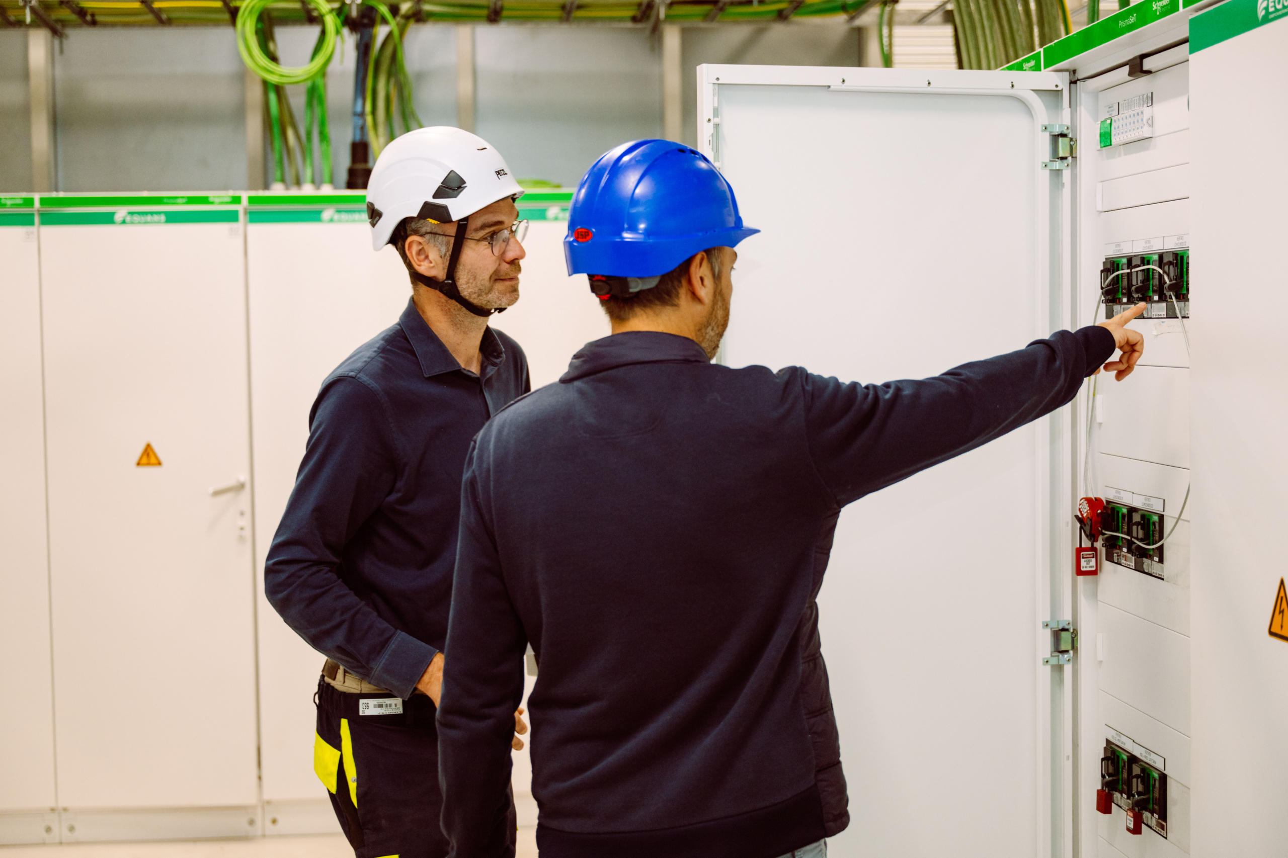 Twee ingenieurs met helm inspecteren een elektrisch verdeelbord