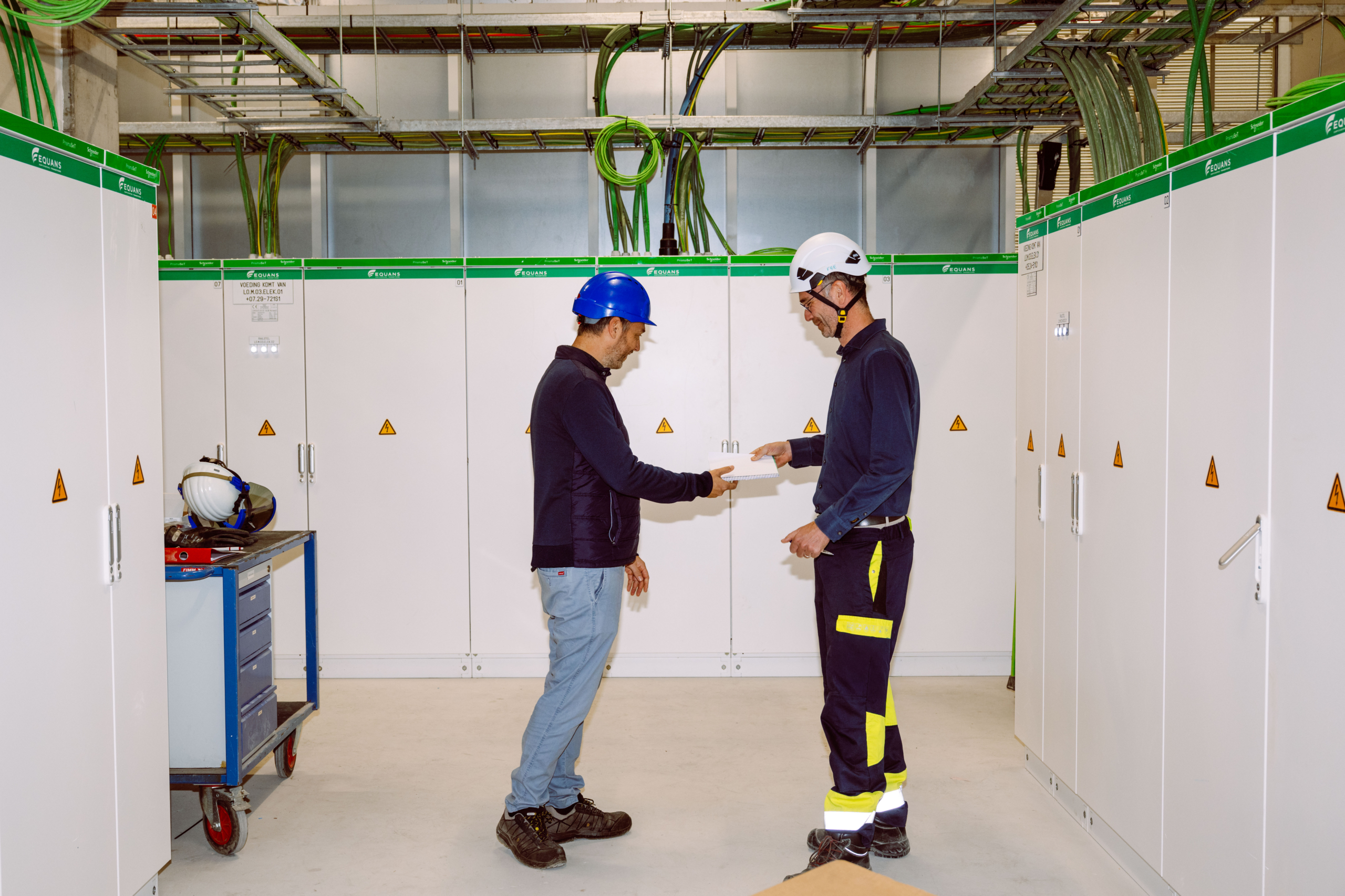 Twee ingenieurs met helm overleggen tussen elektrische verdeelkasten