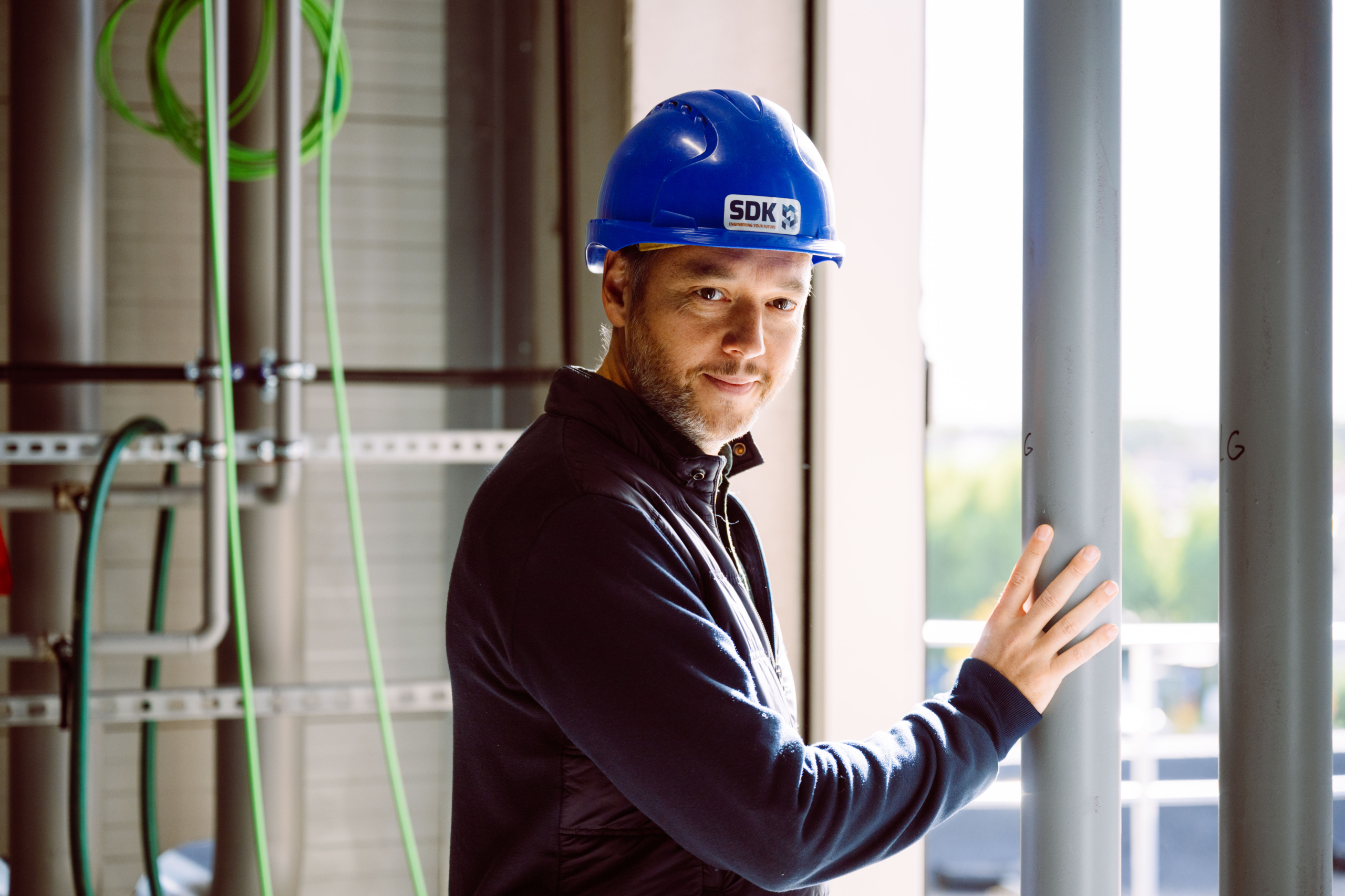 Ingenieur met blauwe helm op de werf, kijkend in de lens